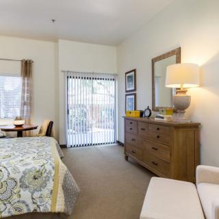 A cozy bedroom with a neatly arranged bed, dresser, and mirror, featuring warm lighting and soft decor.