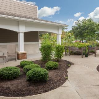 A landscaped outdoor area with bushes and a paved path near a building under a partly cloudy sky.