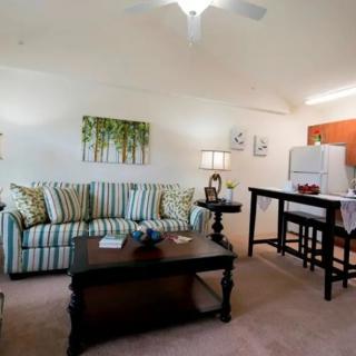 A cozy living room interior with a striped sofa, wooden coffee table, and high bar table with stools, complemented by modern lighting and wall decor.