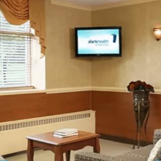 A cozy living room with a wall-mounted television, comfortable seating, and a window with blinds.