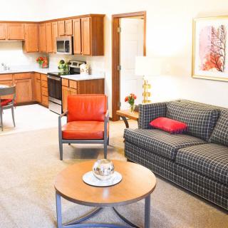 A cozy living room with an open layout connecting to the kitchen, featuring comfortable seating and warm lighting.