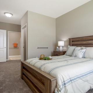 A modern bedroom interior featuring a wooden bed, lamp, and soft carpeting.