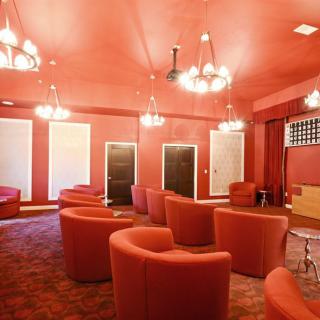 A cozy lounge with red walls and matching seating, illuminated by elegant chandeliers.