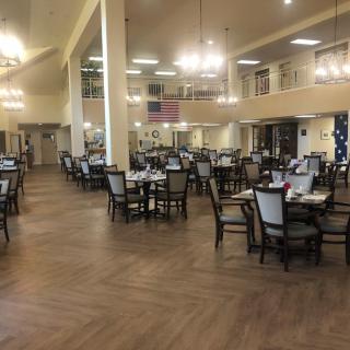 A spacious dining hall with neatly arranged tables and chairs under elegant chandeliers.