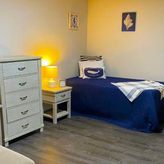 A cozy bedroom with a single bed, nightstand, and dresser, softly lit by a lamp.
