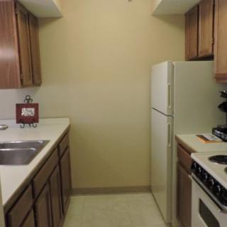 A compact kitchen with wooden cabinets, a refrigerator, and a stove.