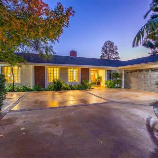 A well-lit house with a spacious driveway surrounded by trees during the evening.