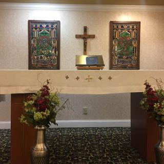 A serene altar setup with a cross and decorative art, surrounded by floral arrangements.