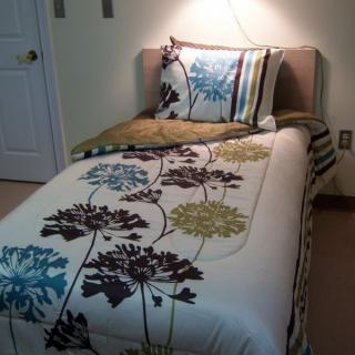 A neatly made single bed with a floral patterned bedspread and matching pillow in a cozy bedroom setting.