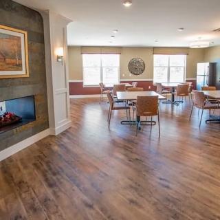 A cozy dining space with wooden floor, featuring a fireplace and ample natural light from large windows.