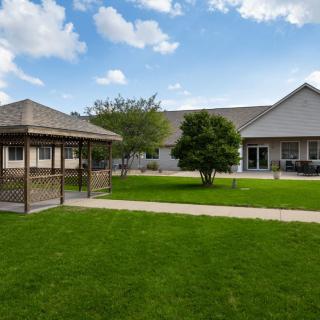 A spacious backyard with a gazebo, lush lawn, and a house under a partly cloudy sky.