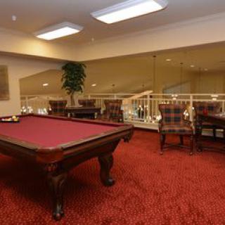 A luxurious billiard room featuring a pool table with red felt, elegant chairs, and plush red carpeting.
