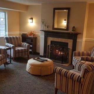A cozy living room with a fireplace, surrounded by striped chairs and an ottoman.