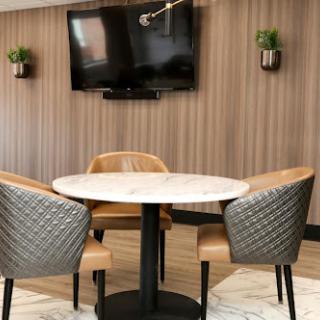 A modern dining area featuring a round marble table and stylish chairs, with a wall-mounted TV in the background.