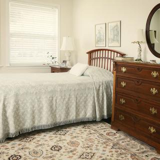 A cozy bedroom with a wooden bed and dresser, featuring a large mirror and patterned carpet.