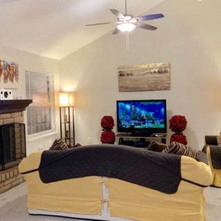 A cozy living room featuring a couch facing a television, with a fireplace on the side and various decor elements like lamps and artwork.