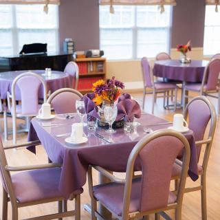 A cozy dining room with purple-themed table settings and a piano in the background.