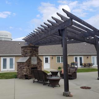 A cozy outdoor patio area featuring a pergola and a stone fireplace, surrounded by comfortable seating.