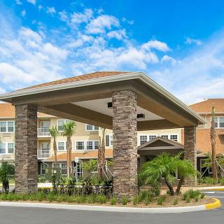 A modern building entrance with stone columns and palm tree landscaping under a partly cloudy sky.
