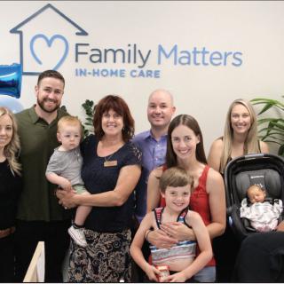 A group of adults and children posing together in front of a 'Family Matters In-Home Care' sign.