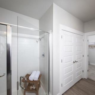 A modern bathroom with a glass shower door, wooden bench, and neatly folded towels.