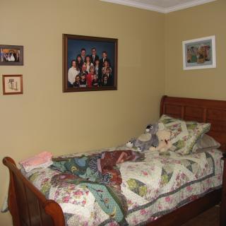 A cozy bedroom with a single bed adorned with a colorful quilt and pillows, complemented by family photos decorating the walls.