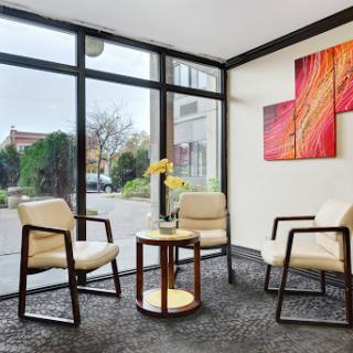 A modern waiting area featuring stylish chairs, a wooden table, and vibrant artwork under natural light.