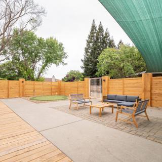 A spacious patio with modern outdoor furniture and a shade sail, surrounded by wooden fencing and trees.