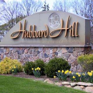 Entrance sign for Hubbard Hill surrounded by blooming daffodils and greenery.