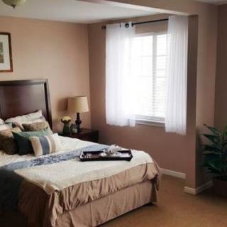 A cozy bedroom with a neatly made bed, bedside lamp, and a window letting in natural light.