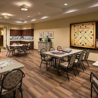 A community game room featuring tables and chairs, with a large Scrabble board on the wall.