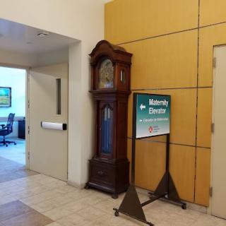 A traditional wooden clock stands beside a directional sign in a modern office interior.
