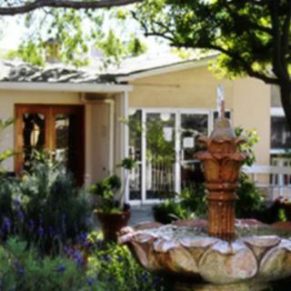 A scenic view of a house entrance with a decorative fountain and lush garden surroundings.