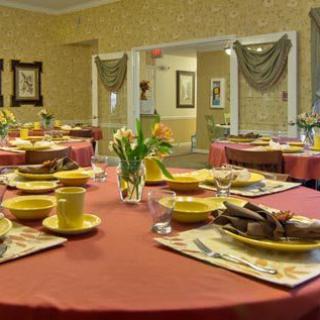 A warmly decorated dining room with tables set for a meal, featuring yellow dinnerware and floral centerpieces.