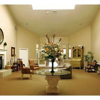 A well-decorated living room featuring a central round table with a floral arrangement, surrounded by elegant furniture and a large mirror.