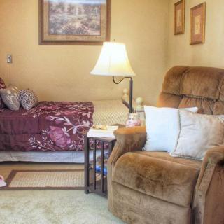 A cozy living room with a comfortable armchair, lamp, and bed.