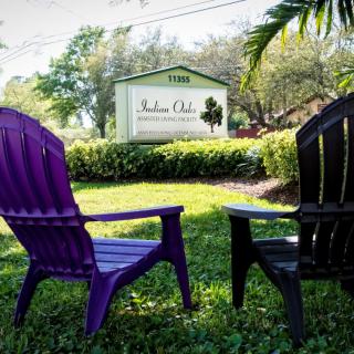 A pair of colorful chairs facing a sign in a lush garden setting.