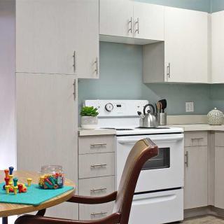 A modern kitchen with white cabinets and a stove, featuring a chair and toys on a table.