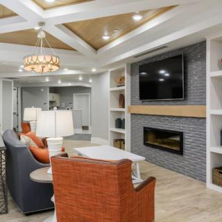 A modern living room featuring a sophisticated ceiling design with recessed lighting, a wall-mounted TV above a sleek fireplace, and comfortable seating arrangements.