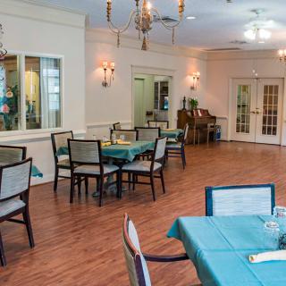 An elegant dining room with neatly arranged tables and chairs, featuring chandeliers and a wooden floor.