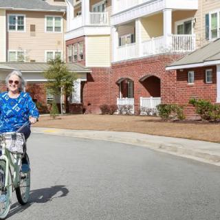 An elderly person riding a bicycle in a residential area on a sunny day.