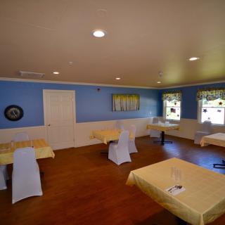 A cozy dining room with blue walls, yellow table settings, and a wooden floor.