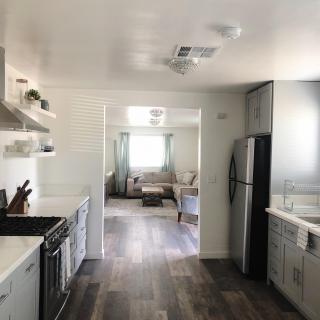 A modern kitchen with hardwood floors, white cabinetry, and stainless steel appliances leading into a bright living room.