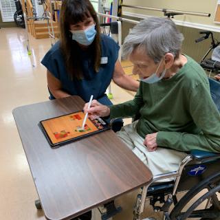 A caregiver assists an elderly person with a tablet, promoting engagement and interaction.