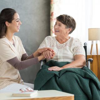 A caregiver smiling and holding the hand of an elderly woman in a wheelchair.