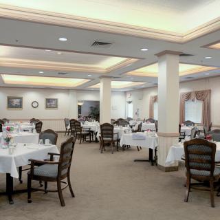 An elegant dining room with neatly set tables and chairs, featuring warm lighting.