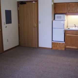 A small apartment interior featuring a kitchenette with wooden cabinets and appliances.