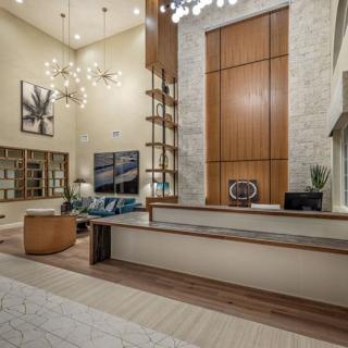 A spacious modern living room with high ceilings, featuring elegant chandeliers, wood paneling, and a stone accent wall. Stylish shelves and comfortable furniture enhance the contemporary design.
