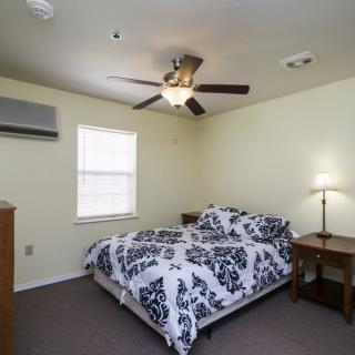 A cozy bedroom with a patterned bedspread, ceiling fan, and a nightstand lamp.