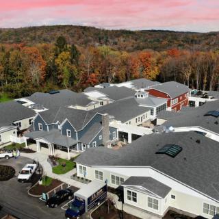 Aerial view of a suburban neighborhood surrounded by autumn foliage under a pink sunset sky.